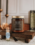 Candle with 'Slow Burn' label on a wooden stand, surrounded by books and candles.
