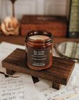 Candle labeled 'Slow Burn' on a wooden stand with books and writing utensils in the background.