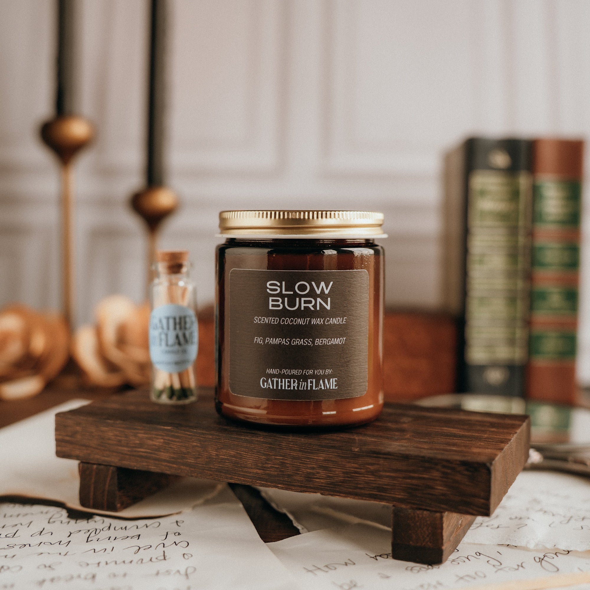 Candle labeled 'Slow Burn' on a wooden stand with books and candles in the background.