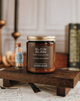 Candle labeled 'Slow Burn' on a wooden stand with books and candles in the background.