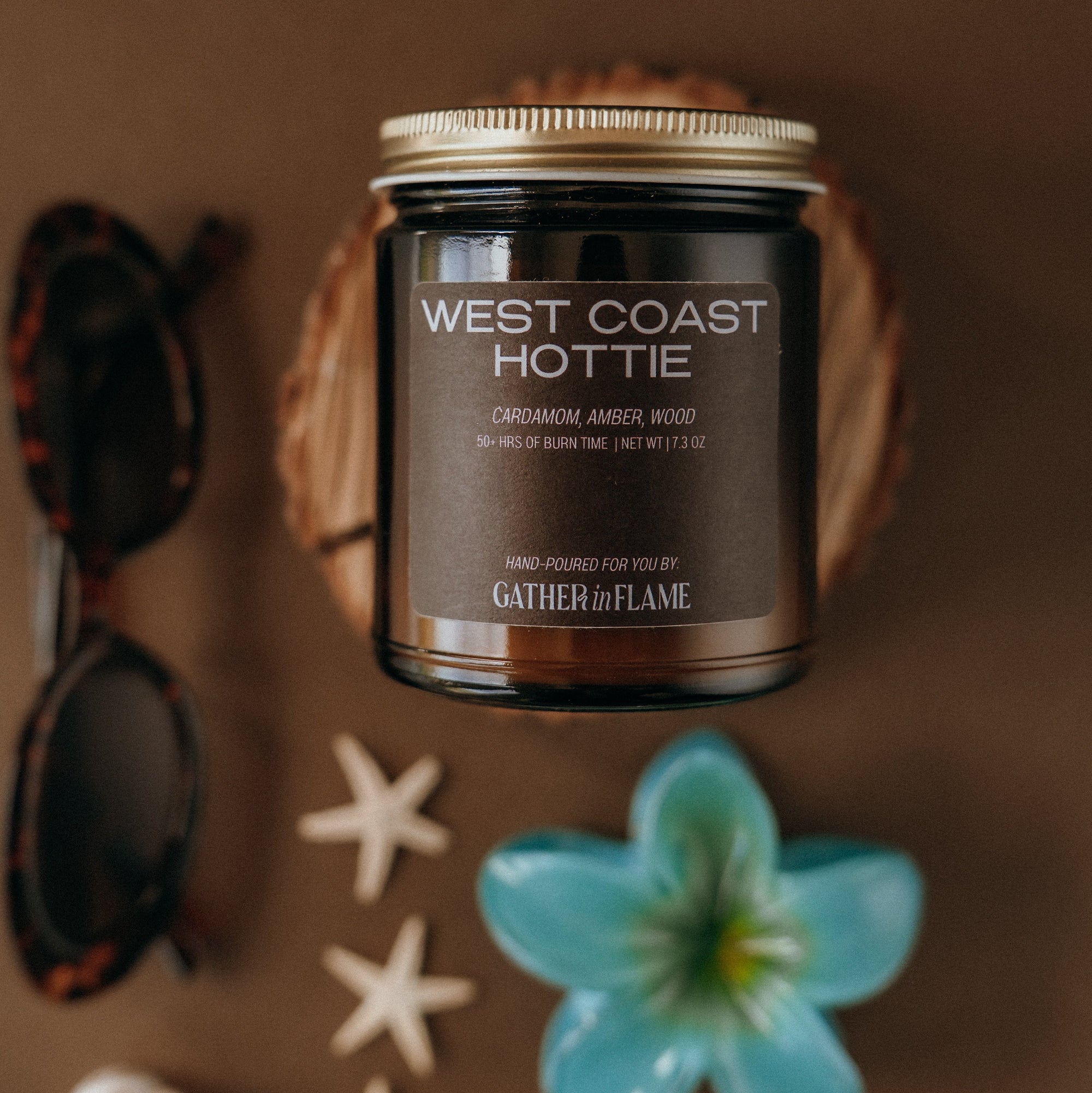 Candle labeled 'West Coast Hottie' with decorative items on a brown background
