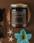 Candle labeled 'West Coast Hottie' with decorative items on a brown background