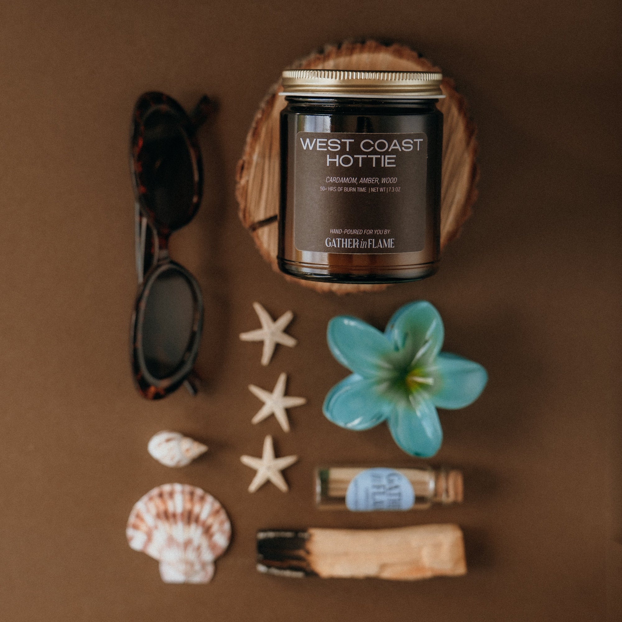 Candle labeled 'West Coast Hottie' surrounded by decorative items on a brown background