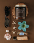 Candle labeled 'West Coast Hottie' surrounded by decorative items on a brown background