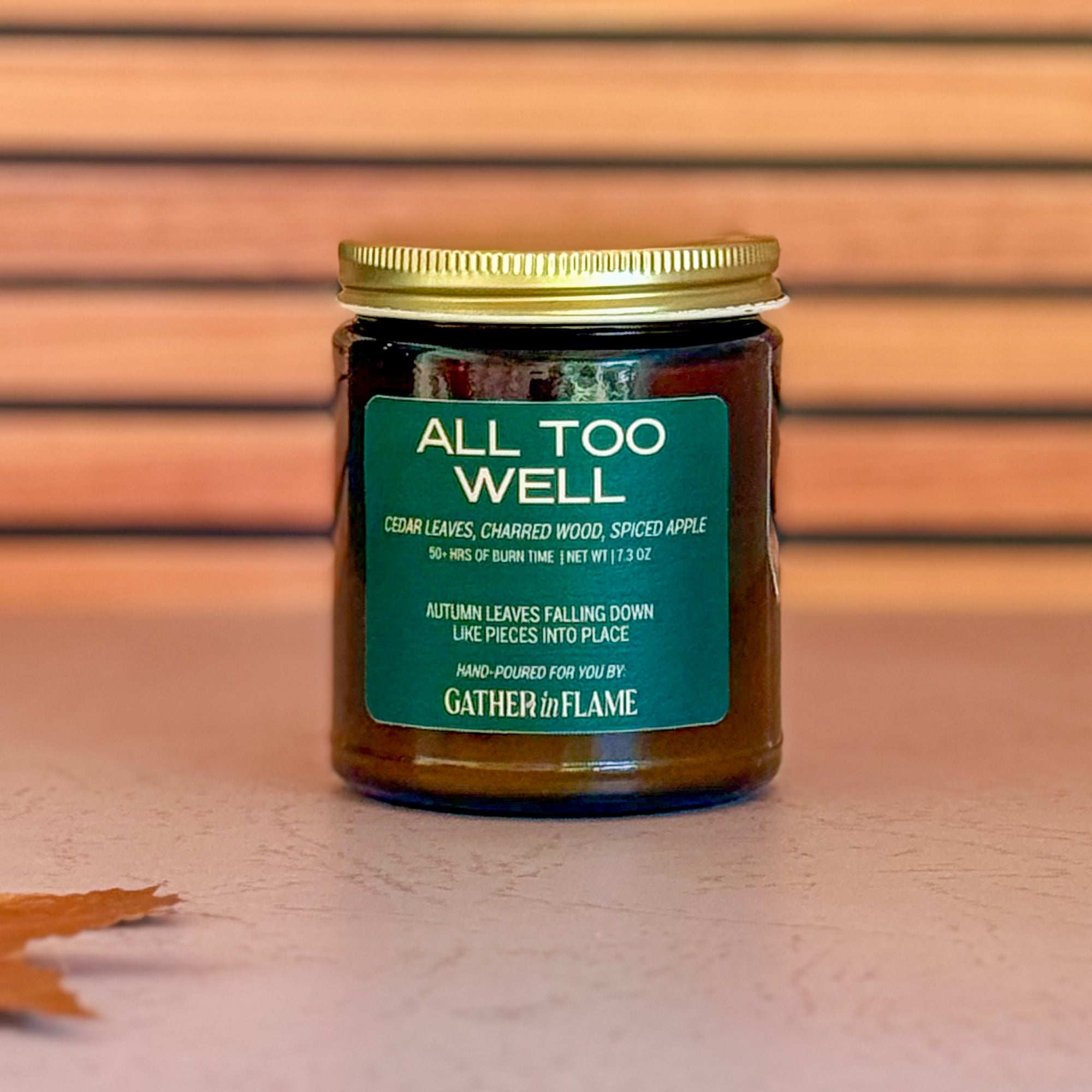 Jar of candle labeled 'All Too Well' with a gold lid on a wooden surface.