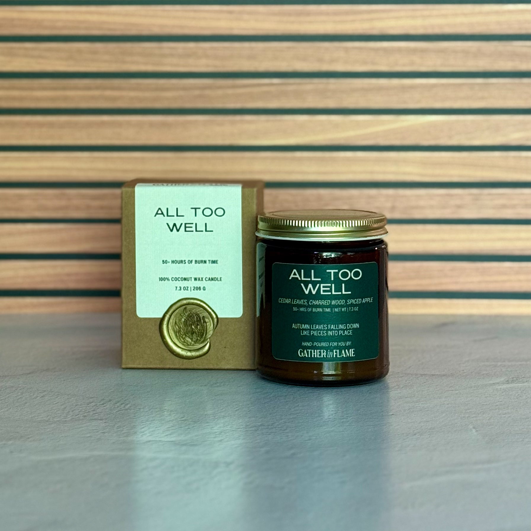 Candle labeled 'All Too Well' with packaging on a wooden surface