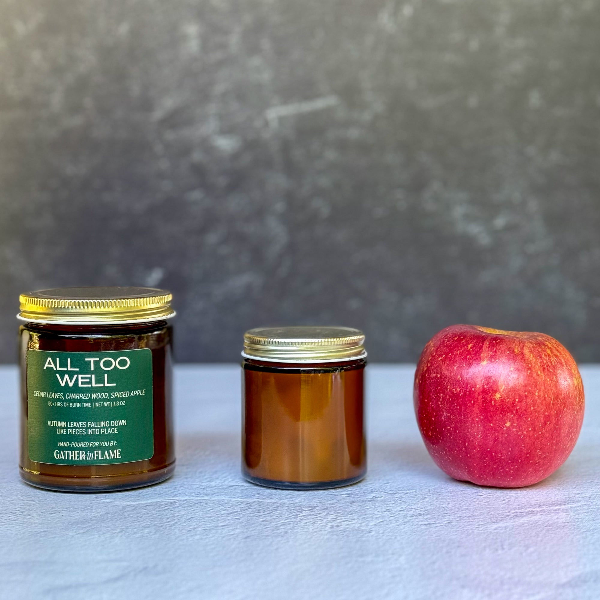 Two candles of different sizes and an apple on a textured surface with a gray background