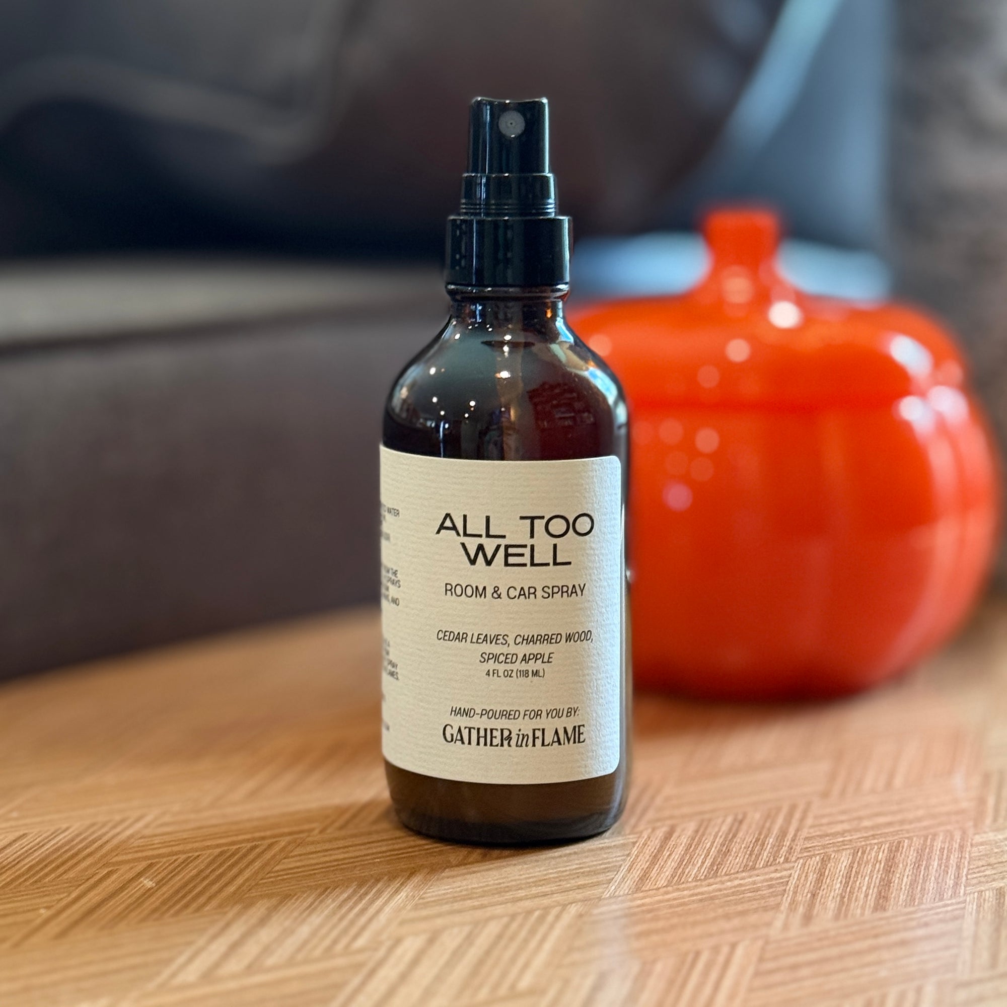 Bottle of 'All Too Well' room and car spray on a wooden surface with an orange ceramic pumpkin in the background.