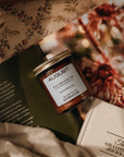 Jar of August candle on a surface with a Gratitude Journal and floral photo in the background