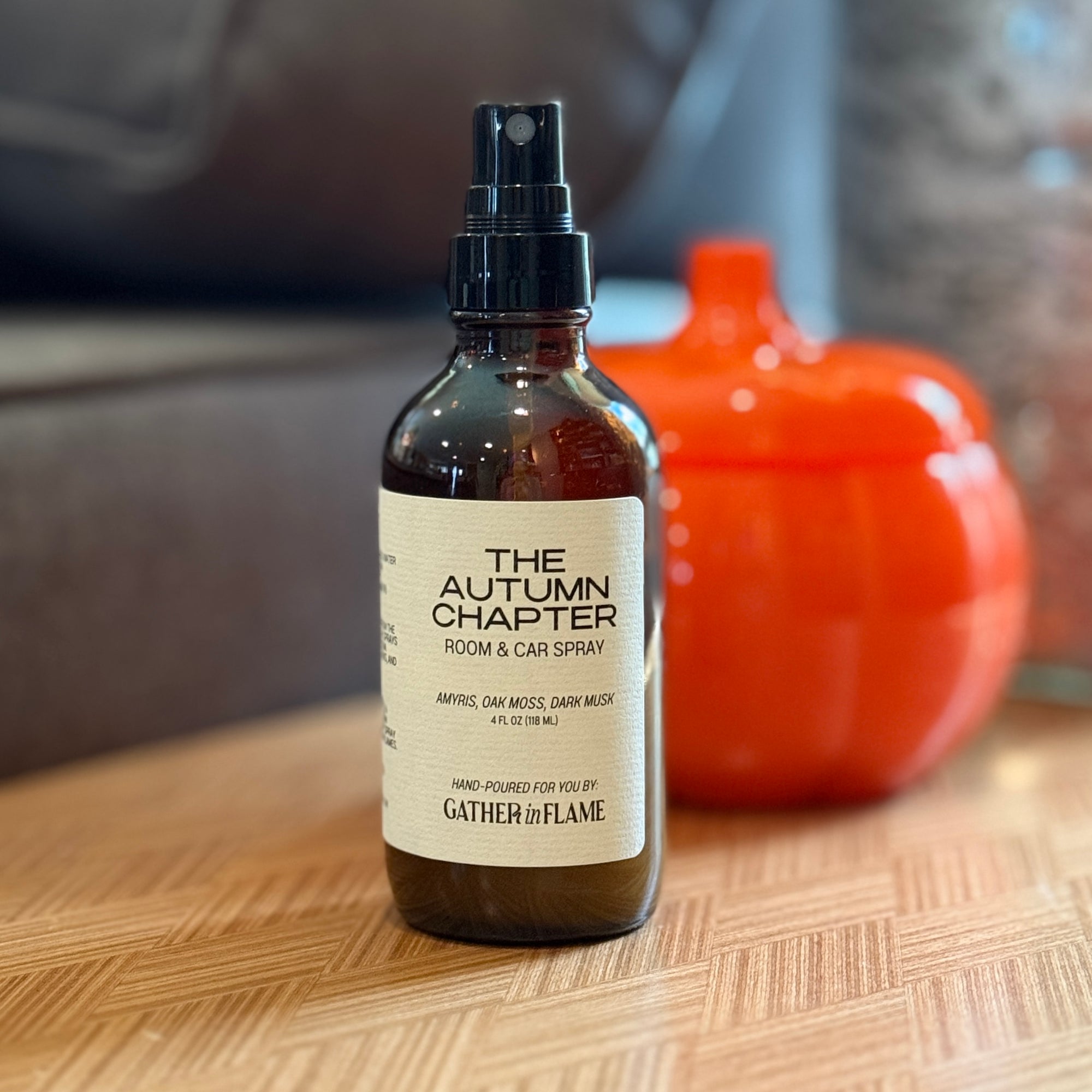 Bottle of 'The Autumn Chapter' room & car spray on a wooden surface with a pumpkin in the background.