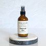 A brown amber spray bottle labeled 'Gather In Flame Candle Co. Beachside Fire Room & Car Spray' placed on a white marble surface.
