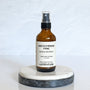 A brown amber spray bottle labeled 'Beachside Fire' by Gather In Flame Candle Co. on a white marble surface.