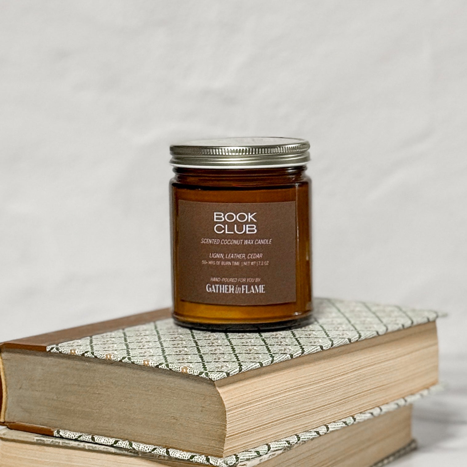 Amber glass jar candle labeled Book Club on a stack of books with a white background.