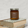 Amber glass jar candle labeled Book Club on a stack of books with a white background.