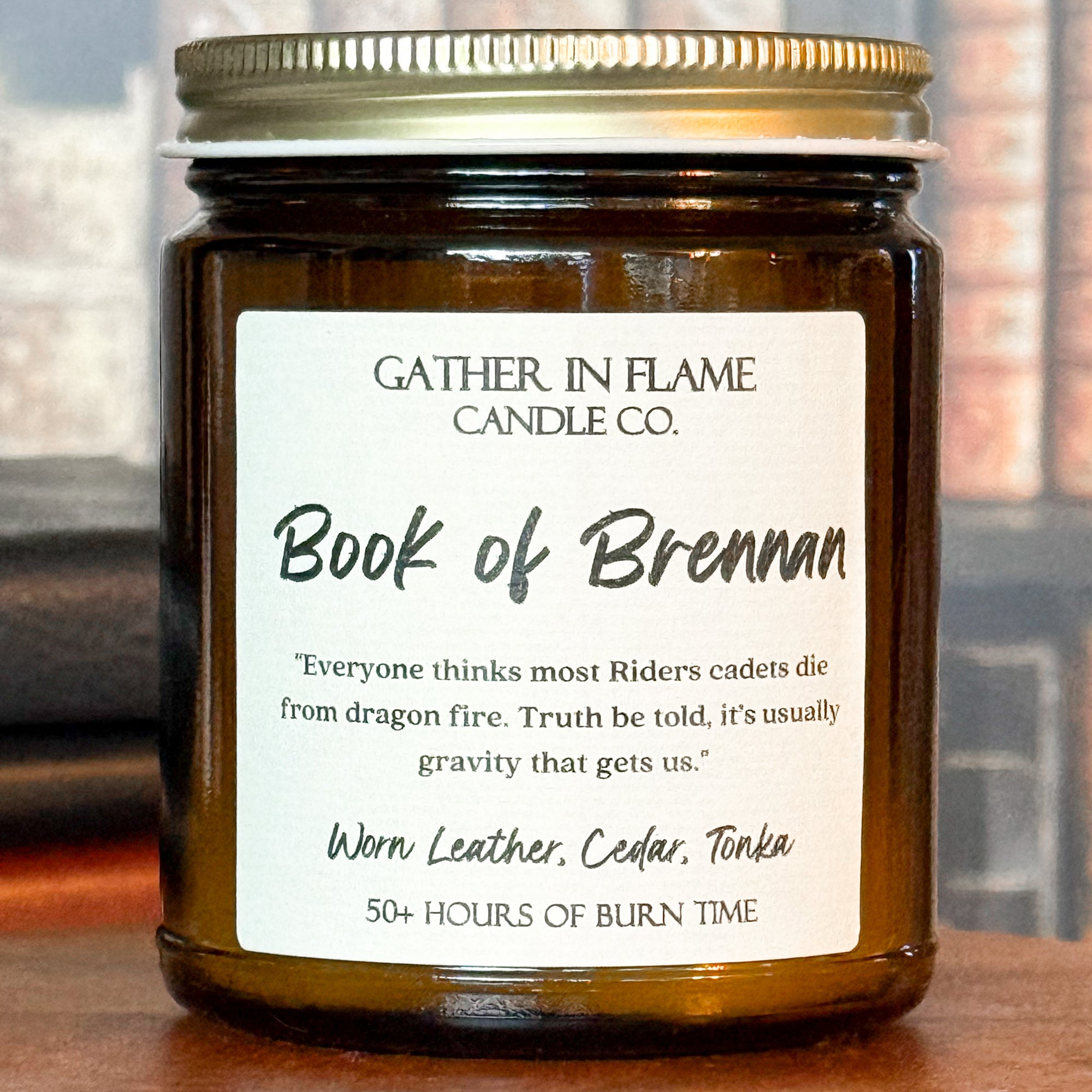 Close up of a jar candle labeled 'Book of Brennan' on a wooden stand, with a background of books.