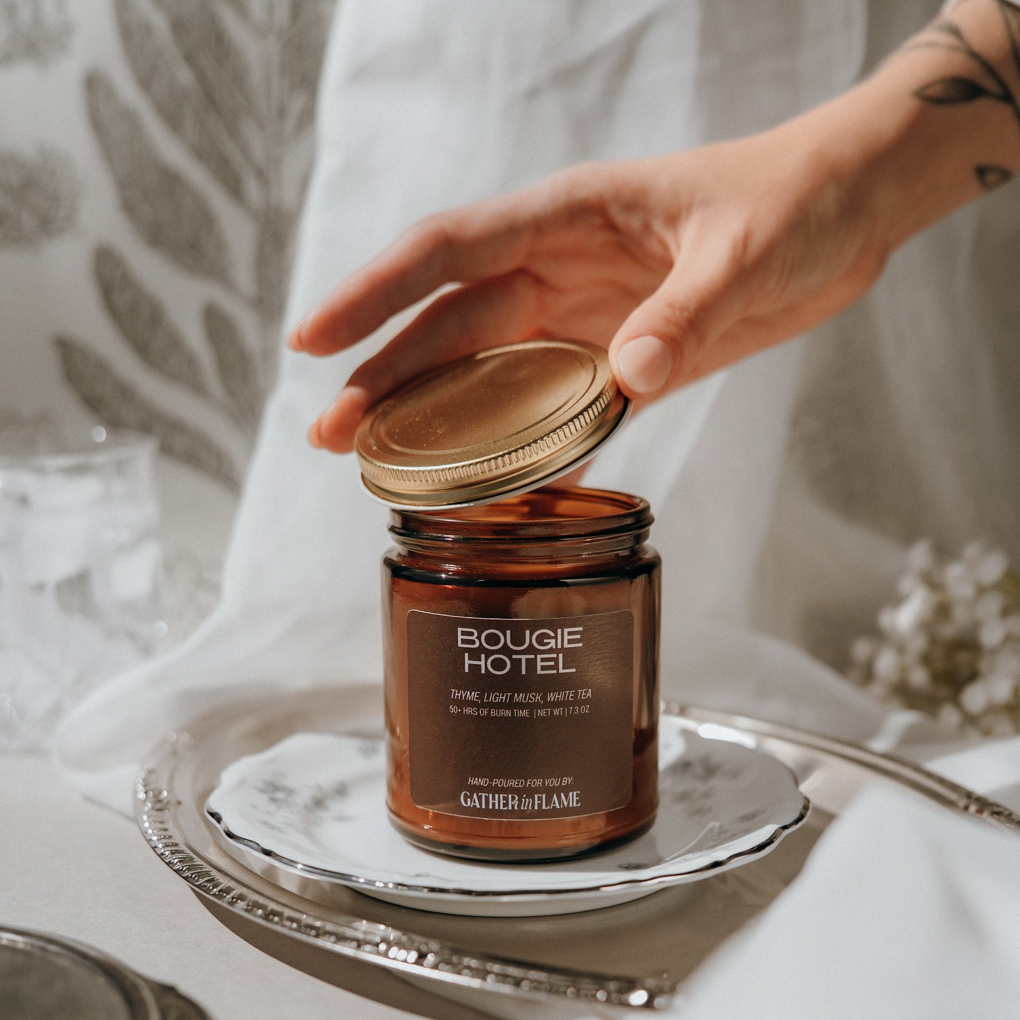 Bougie Hotel candle being held by a hand on a silver tray with a neutral background