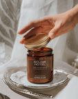 Bougie Hotel candle being held by a hand on a silver tray with a neutral background