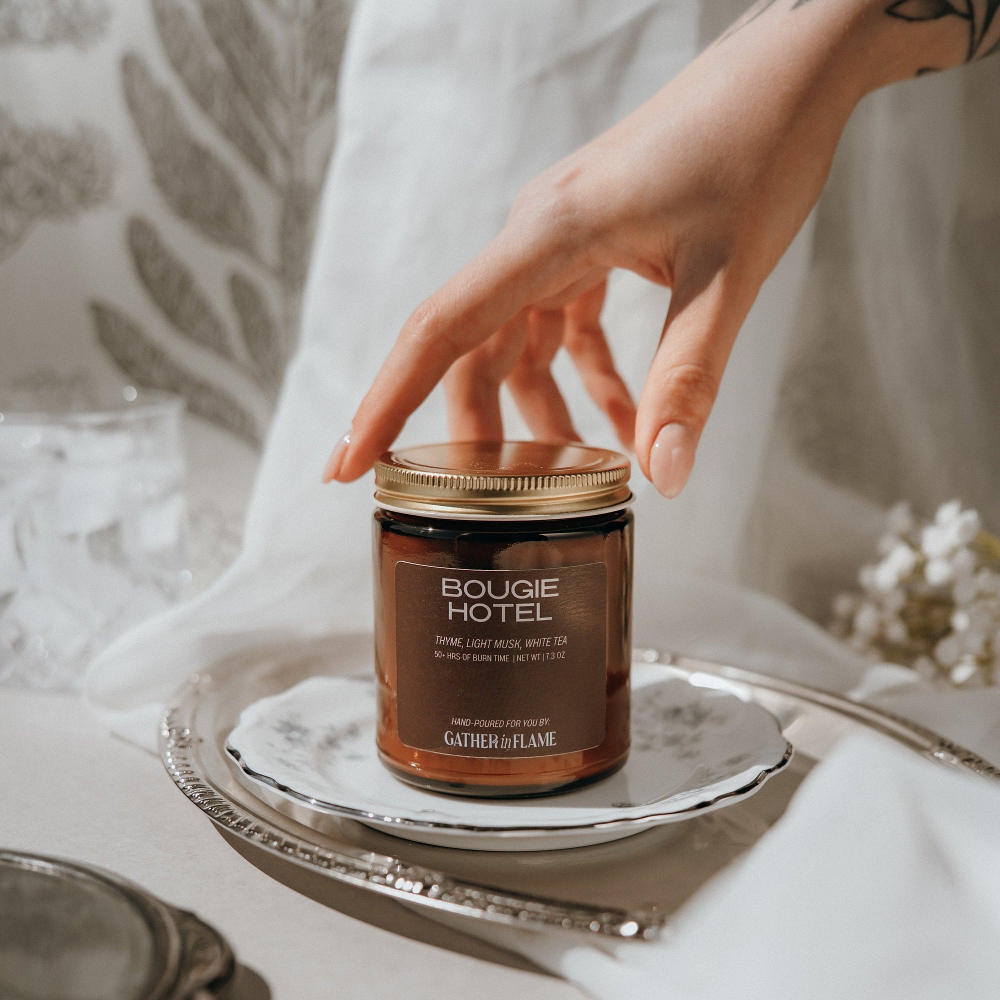 Bouge Hotel candle on a silver tray with a hand reaching towards it