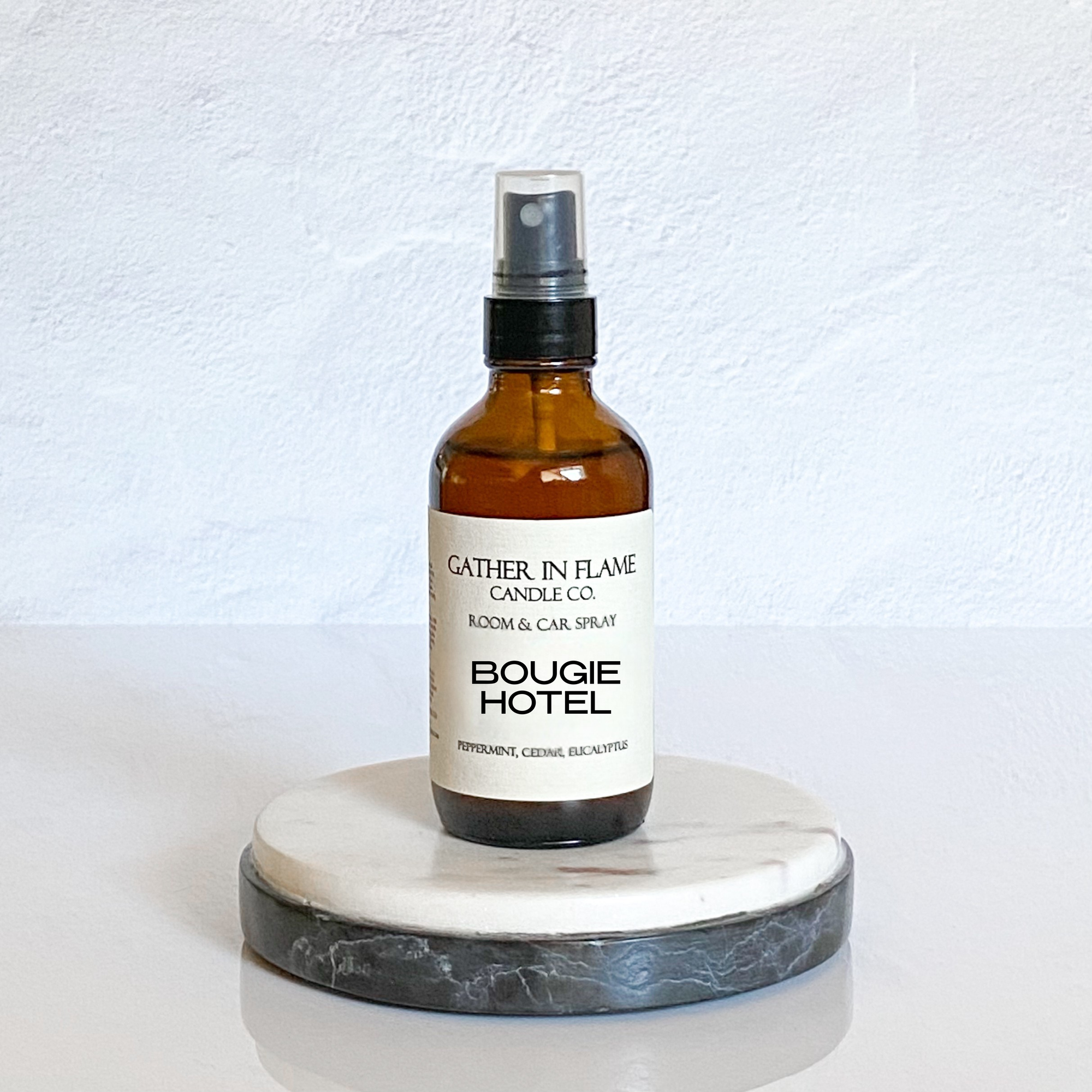 Bottle of 'Bougie Hotel' spray on a marble stand with a white background