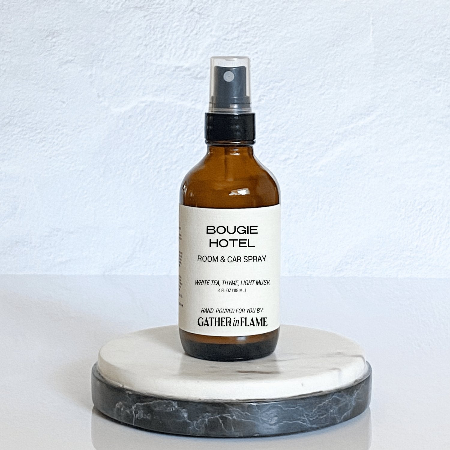 A brown amber spray bottle labeled 'Bougie Hotel' by Gather In Flame Candle Co. on a white marble surface.