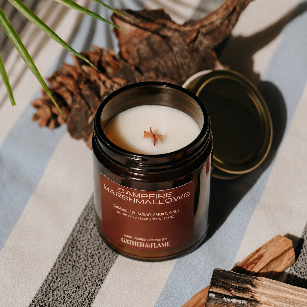 Campfire Marshmallows candle on a striped surface with natural elements.