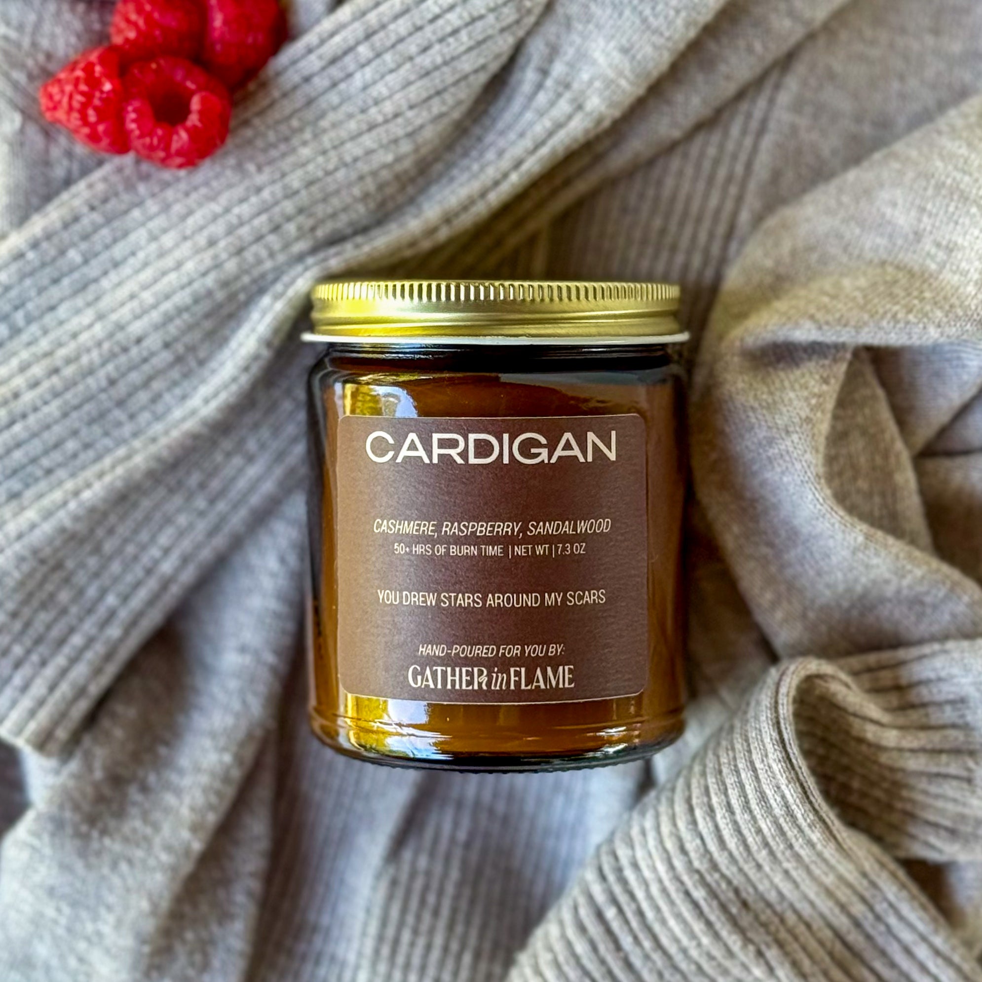 Jar of 'Cardigan' candle on a textured fabric background and raspberries