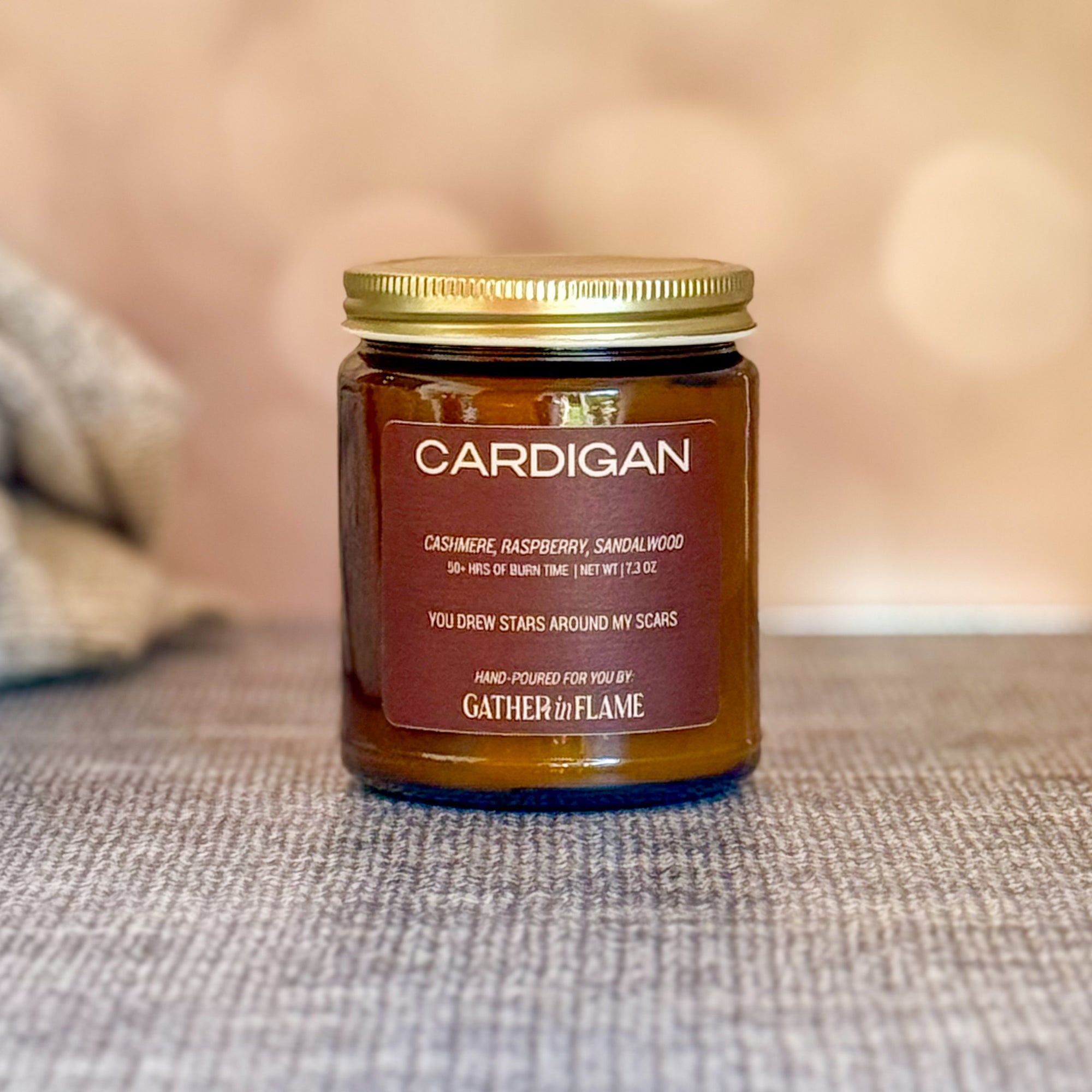 Jar of 'Cardigan' candle with a gold lid on a textured surface.