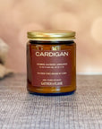 Jar of 'Cardigan' candle with a gold lid on a textured surface.