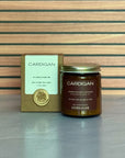Candle jar labeled 'Cardigan' with packaging on a wooden surface