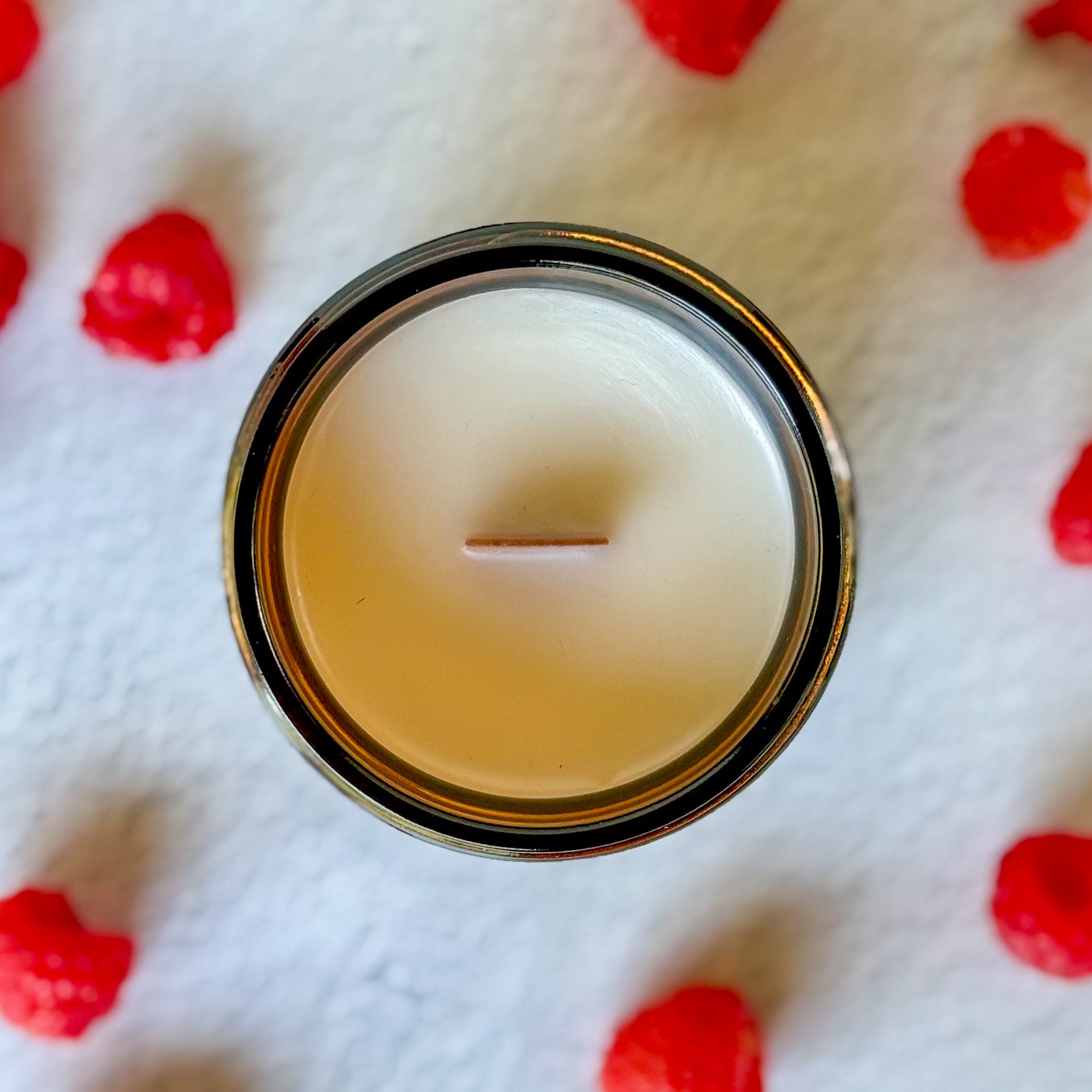 Cardigan candle in a amber glass jar on a white surface with raspberries