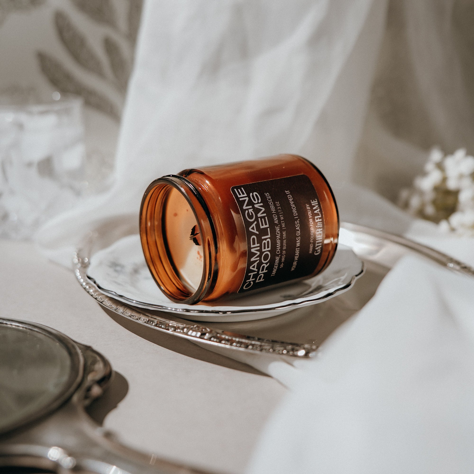 Candle jar labeled 'Champagne Problems' on a white surface with a blurred background