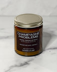 Candle jar labeled 'Champagne Problems' on a marble surface