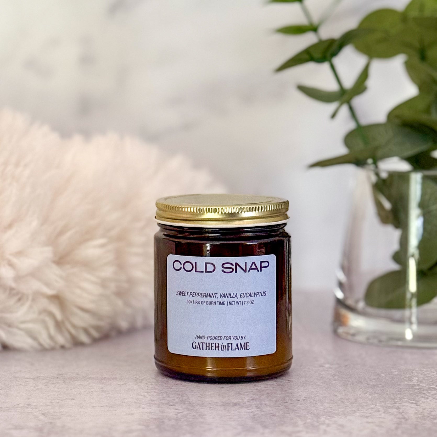 Jar of candle labeled 'Cold Snap' with decorative elements in the background