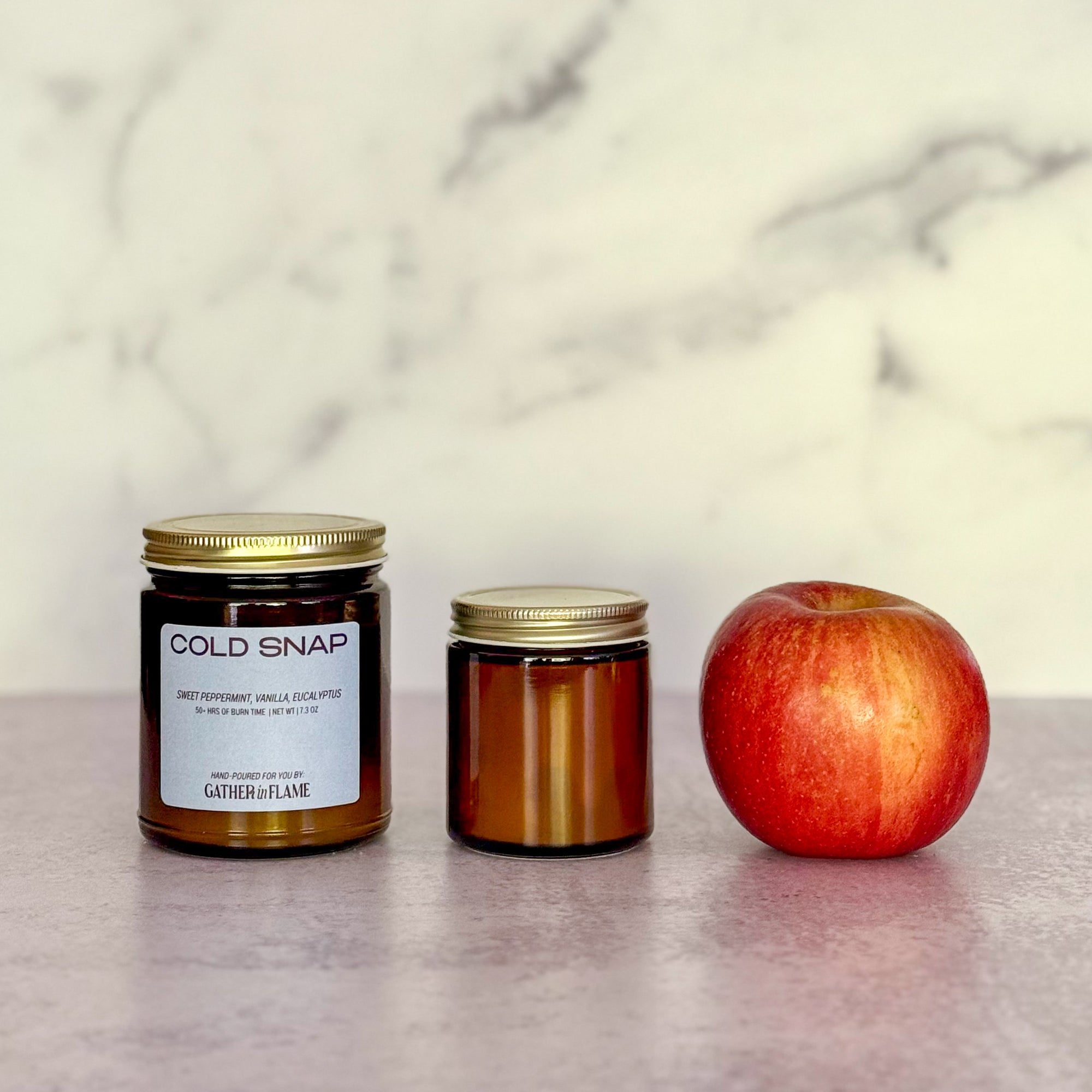 Two candles of different sizes labeled 'Cold Snap' and an apple on a marble surface