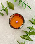 Overhead view of lit candle surface with melted wax surrounded by green leaves on a textured white background