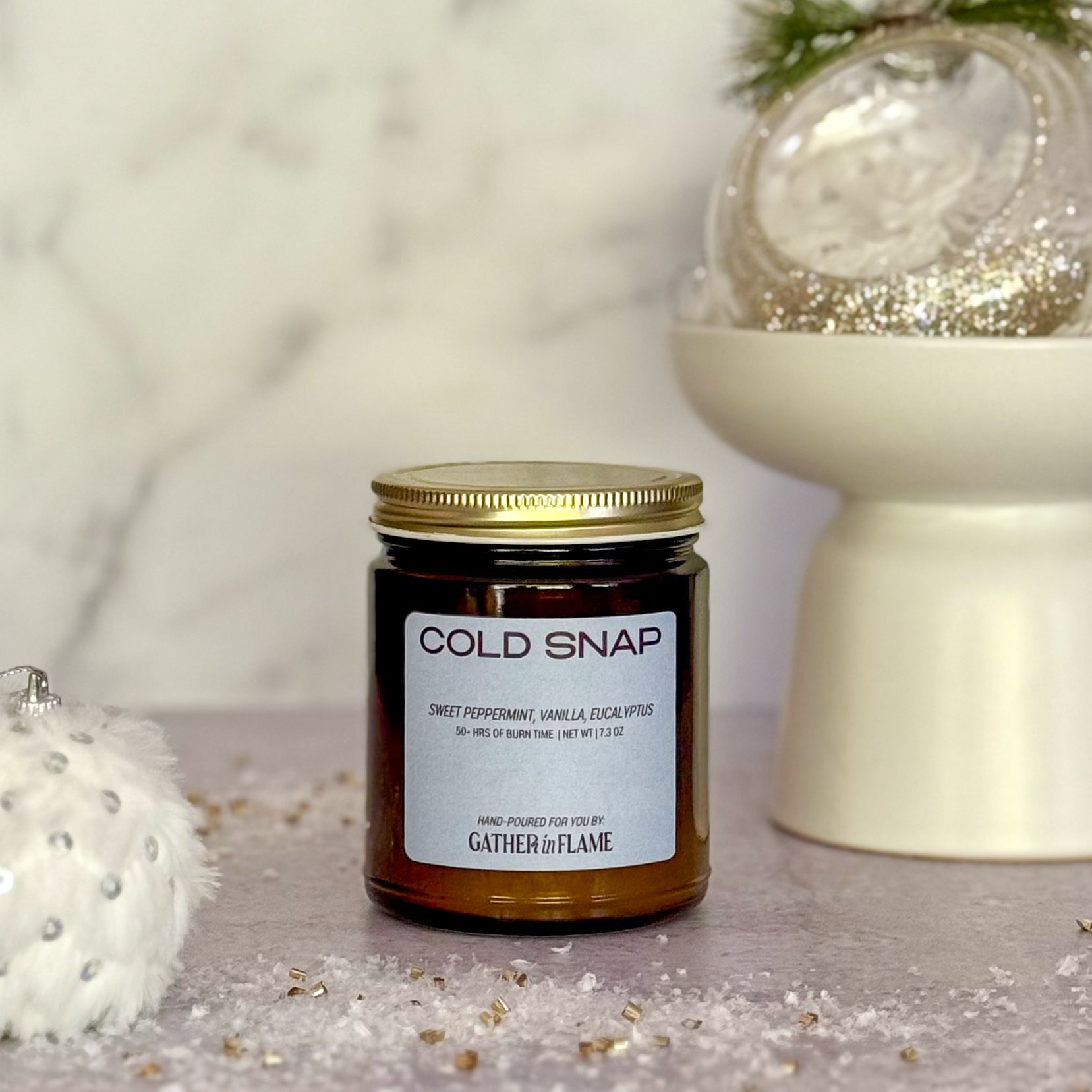 Jar of 'Cold Snap' candle by Gather the Flame on a decorative surface with festive elements.
