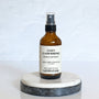 A brown amber spray bottle labeled 'Cozy Cashmere' by Gather In Flame Candle Co. on a white marble surface.