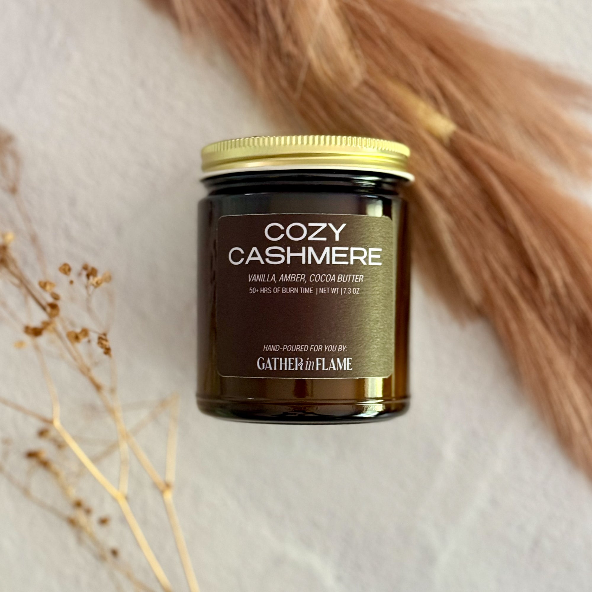 Jar of 'Cozy Cashmere' candle with gold lid on a soft background with dried pampas grass and baby's breath