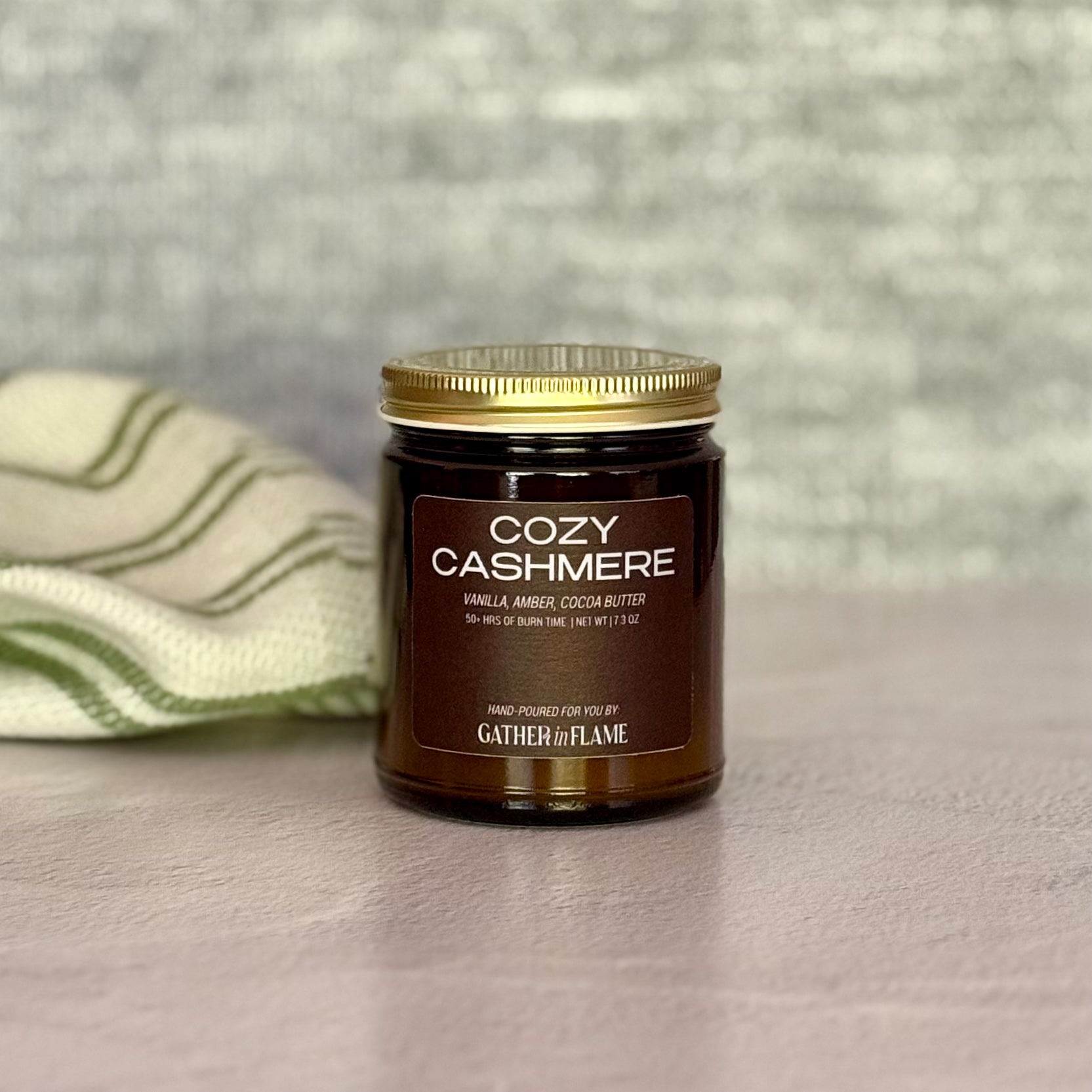 Jar of 'Cozy Cashmere' candle with a gold lid on a neutral background