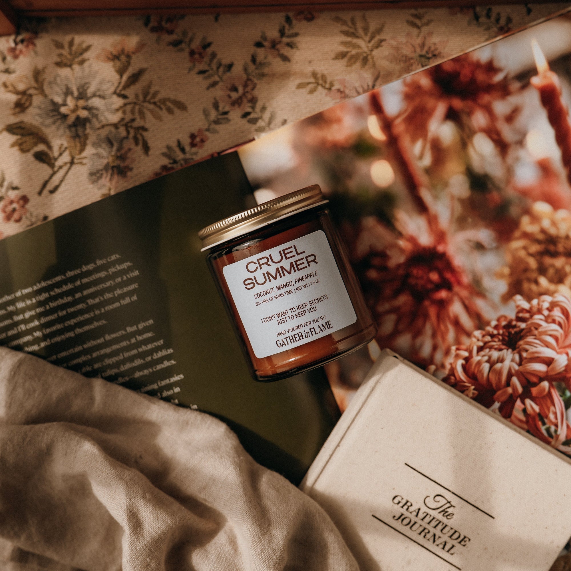 Cruel Summer candle on a floral surface with a book and fabric