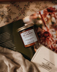 Cruel Summer candle on a floral surface with a book and fabric