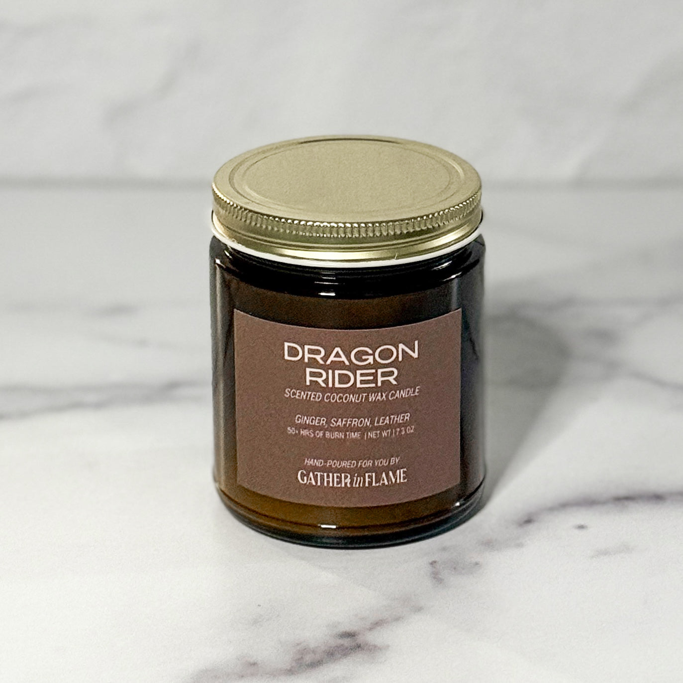 Closeup picture of amber jar candle labeled Dragon Rider with a white background.