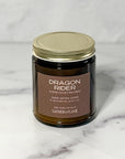 Closeup picture of amber jar candle labeled Dragon Rider with a white background.