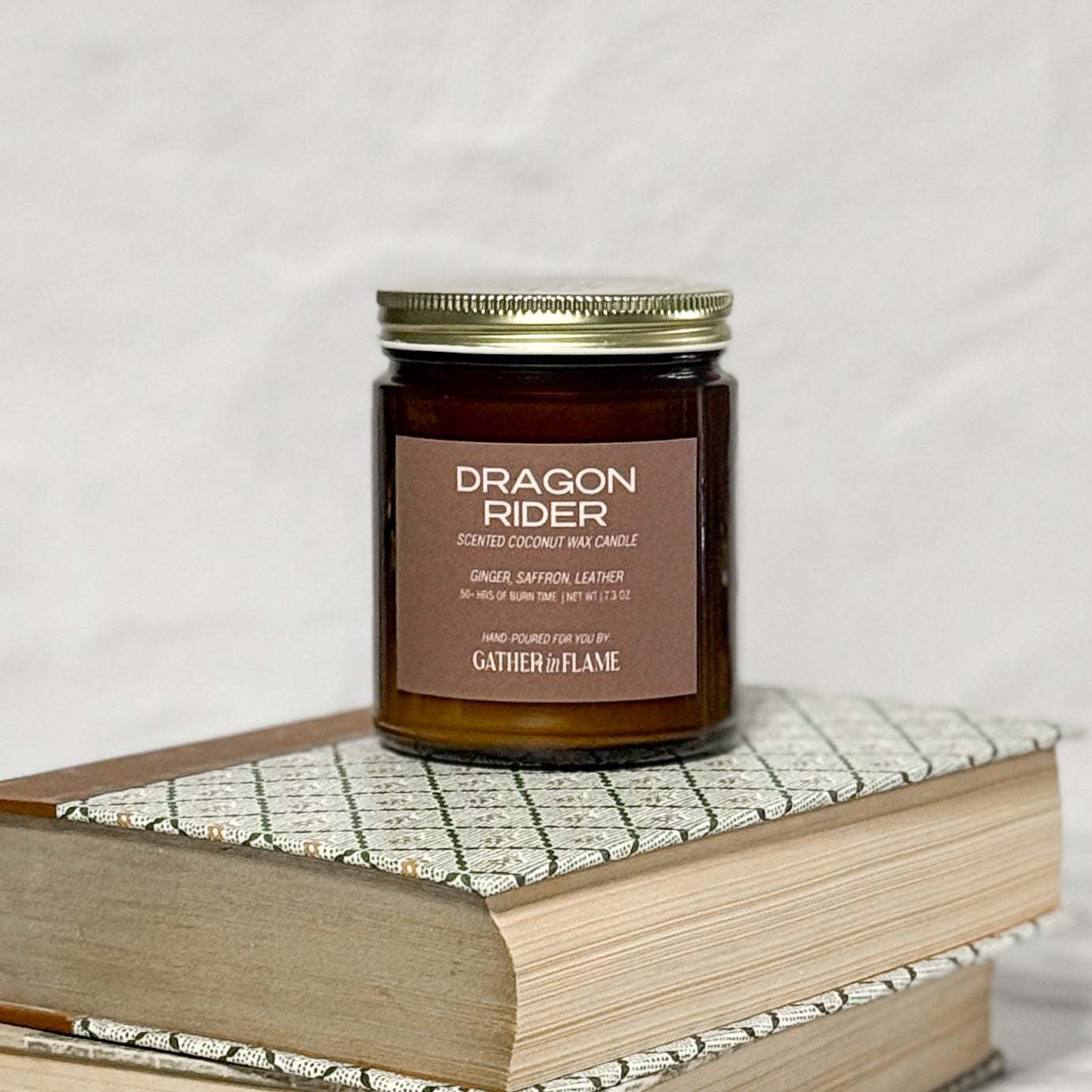 Amber jar candle labeled Dragon Rider on a stack of books with a white background.