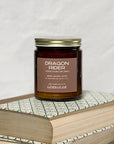 Amber jar candle labeled Dragon Rider on a stack of books with a white background.