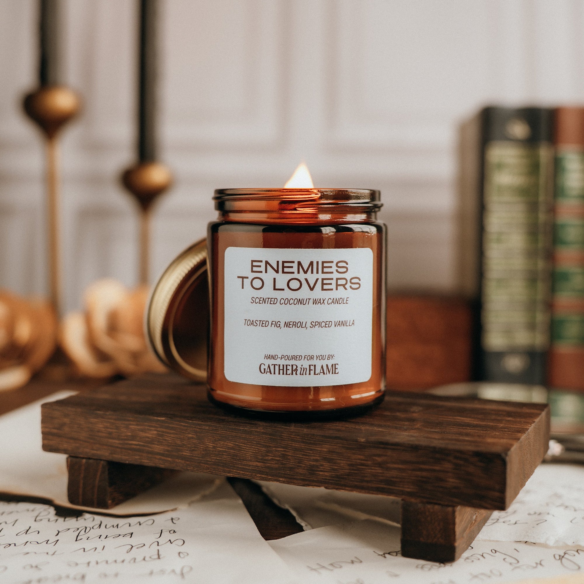 Candle labeled 'Enemies to Lovers' on a wooden stand with books and candles in the background.