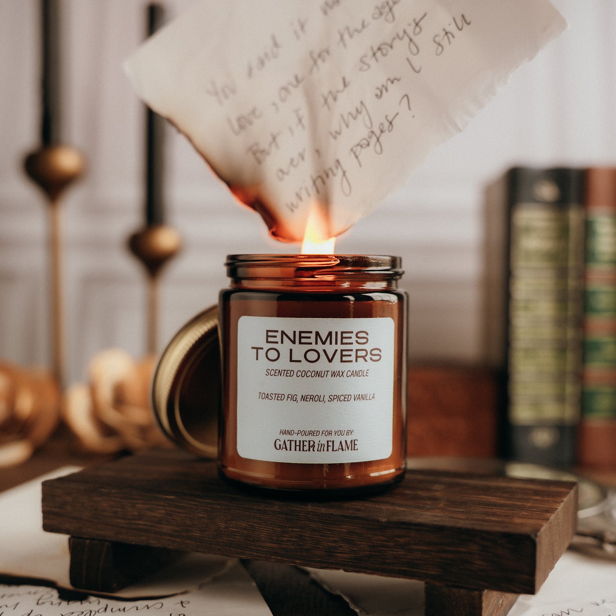 Note being lit with a candle, surrounded by books and candles on a wooden stand.