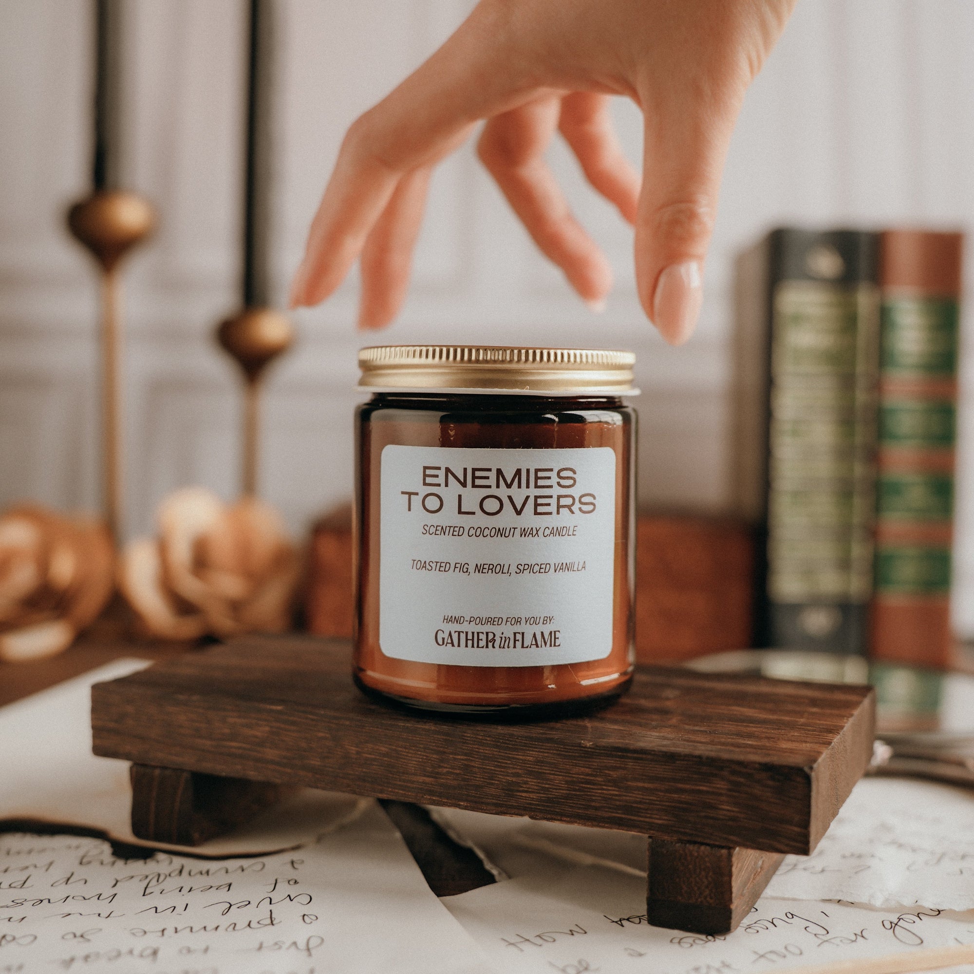 Candle labeled 'Enemies to Lovers' on a wooden stand with a hand reaching towards it.