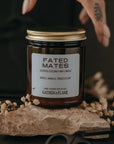 Candle jar labeled 'Fated Mates' with a hand holding it on a dark background
