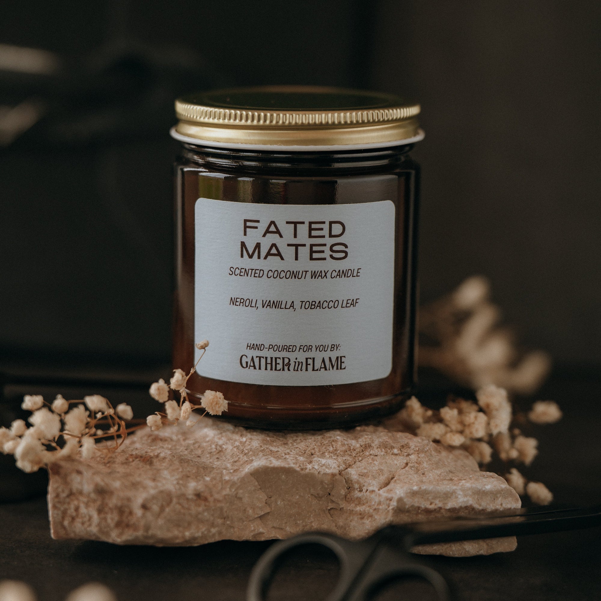 Candle jar labeled 'Fated Mates' on a dark background with dried flowers and scissors.